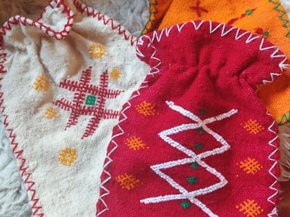 Three handwoven hot water bottle covers in red, orange and undyed wool