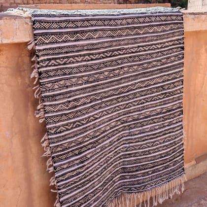 A black and white patterned carpet hanging over an earthen wall