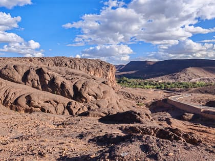 Dark rock ridges outside Ouarzazate, a green line of palms in the valley, table mountains behind